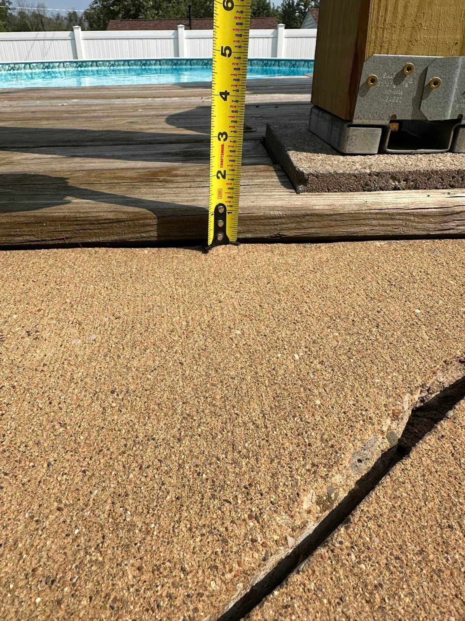 Tape measure shows a 2-inch gap between a wooden deck and textured concrete.