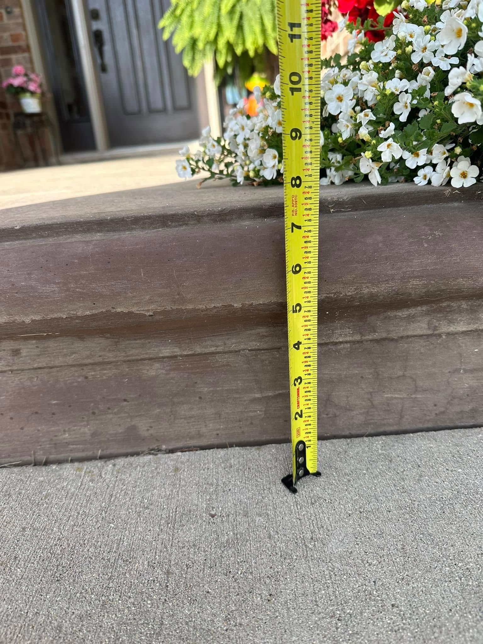 A yellow tape measure showing the height of a concrete step; flowers in background.