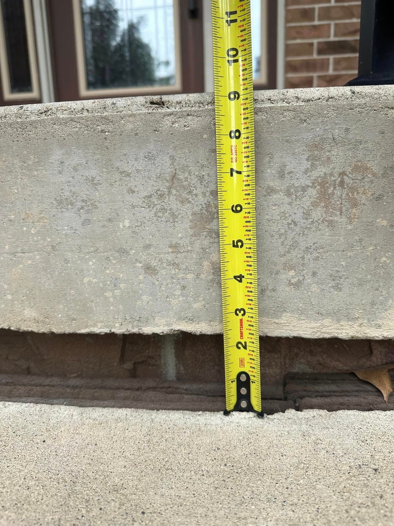 Yellow tape measure showing a 2-inch height difference between concrete steps. Brick building in background.