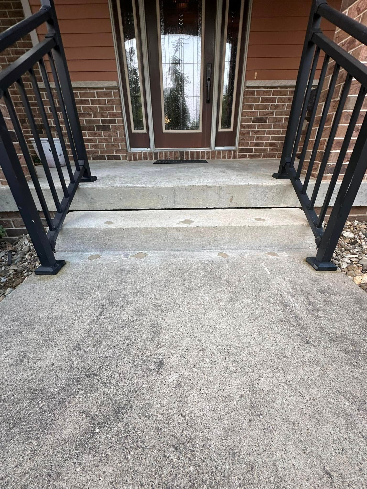 Concrete steps leading up to a front door with black railings on either side.