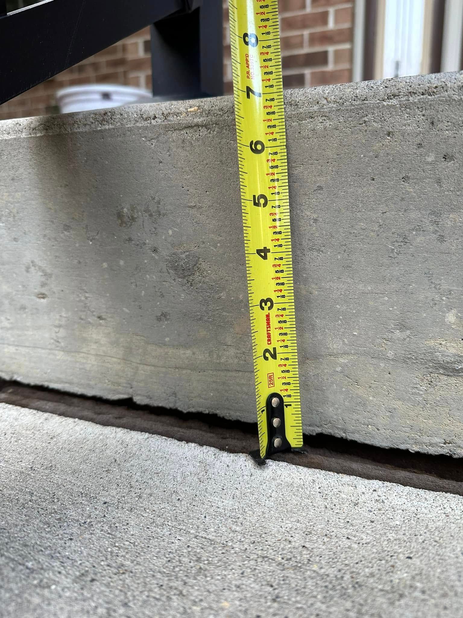 A yellow tape measure showing the height of a concrete step is approximately 3 inches.