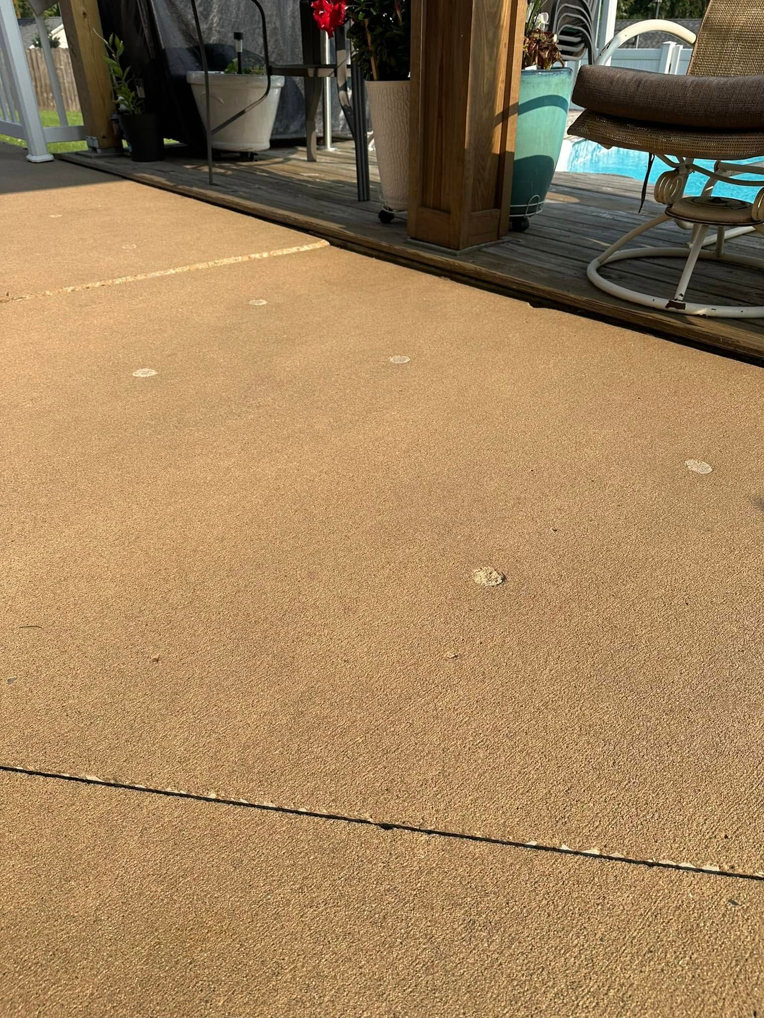 Tan pebble-like patio surface with decorative black border, near plants and pool.