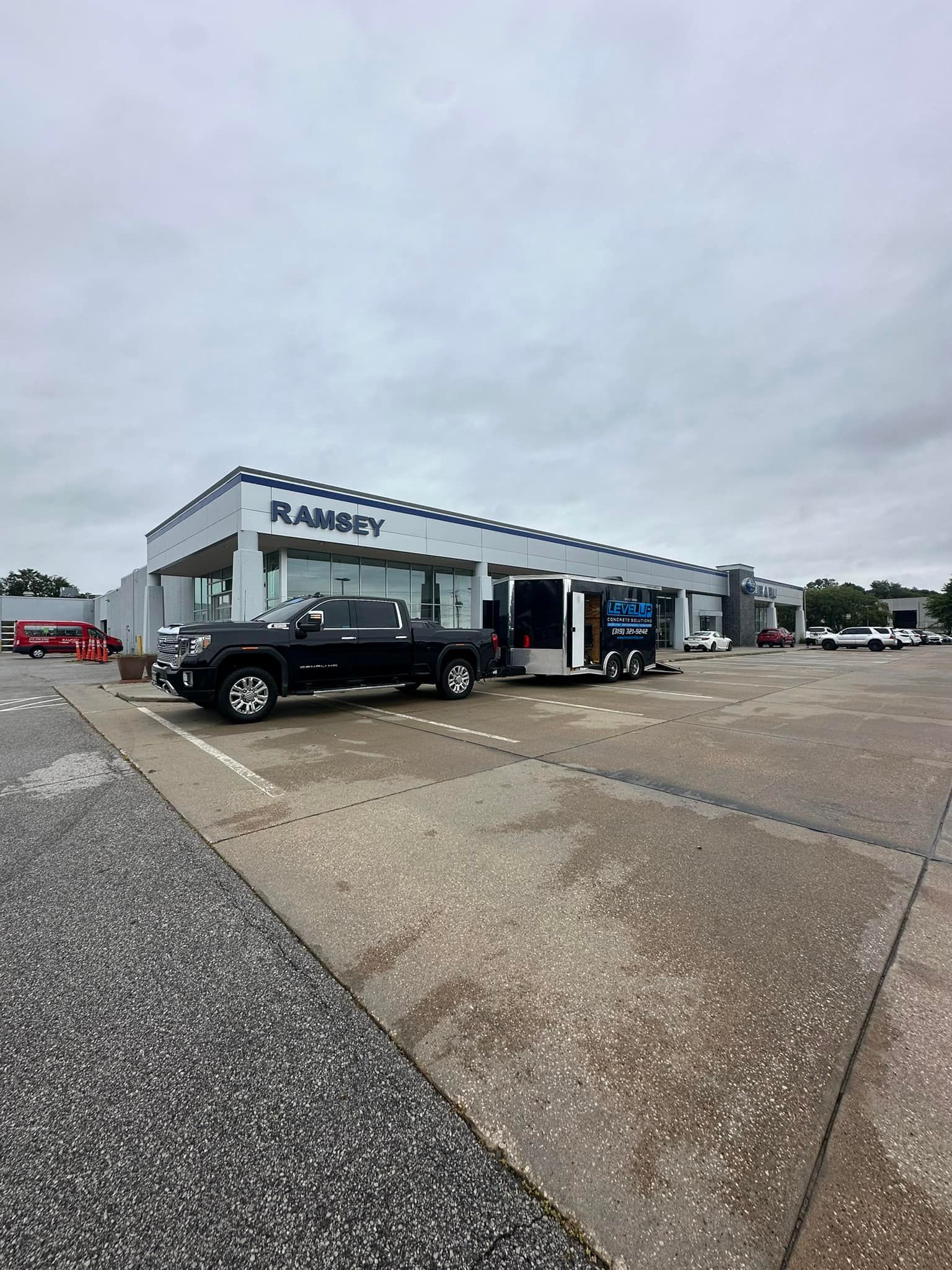 Black truck towing a trailer parked in front of a Ramsey dealership building on an overcast day.