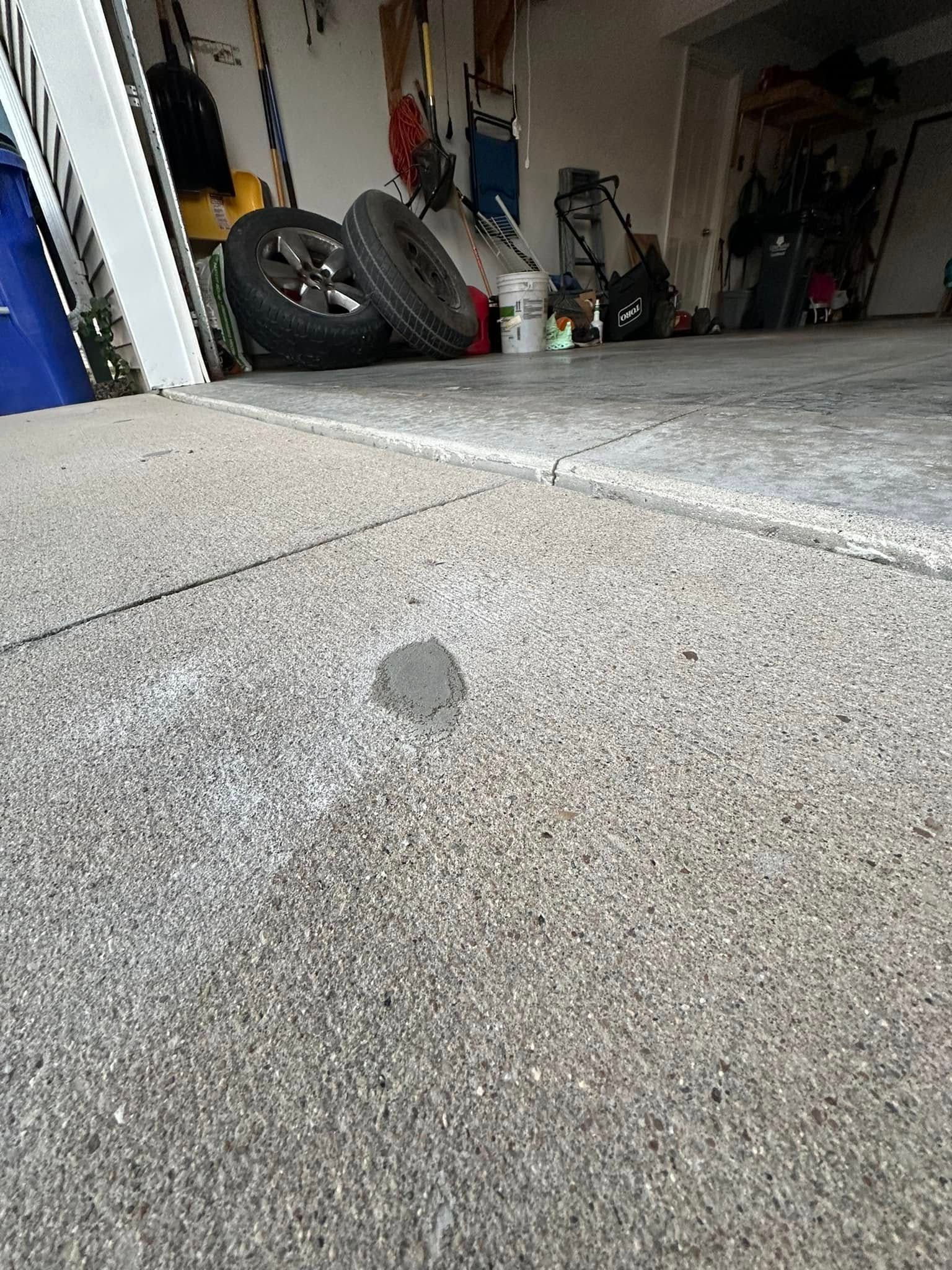 Gray garage floor with a small, gray mound in the center. Tires and tools are visible in the background.
