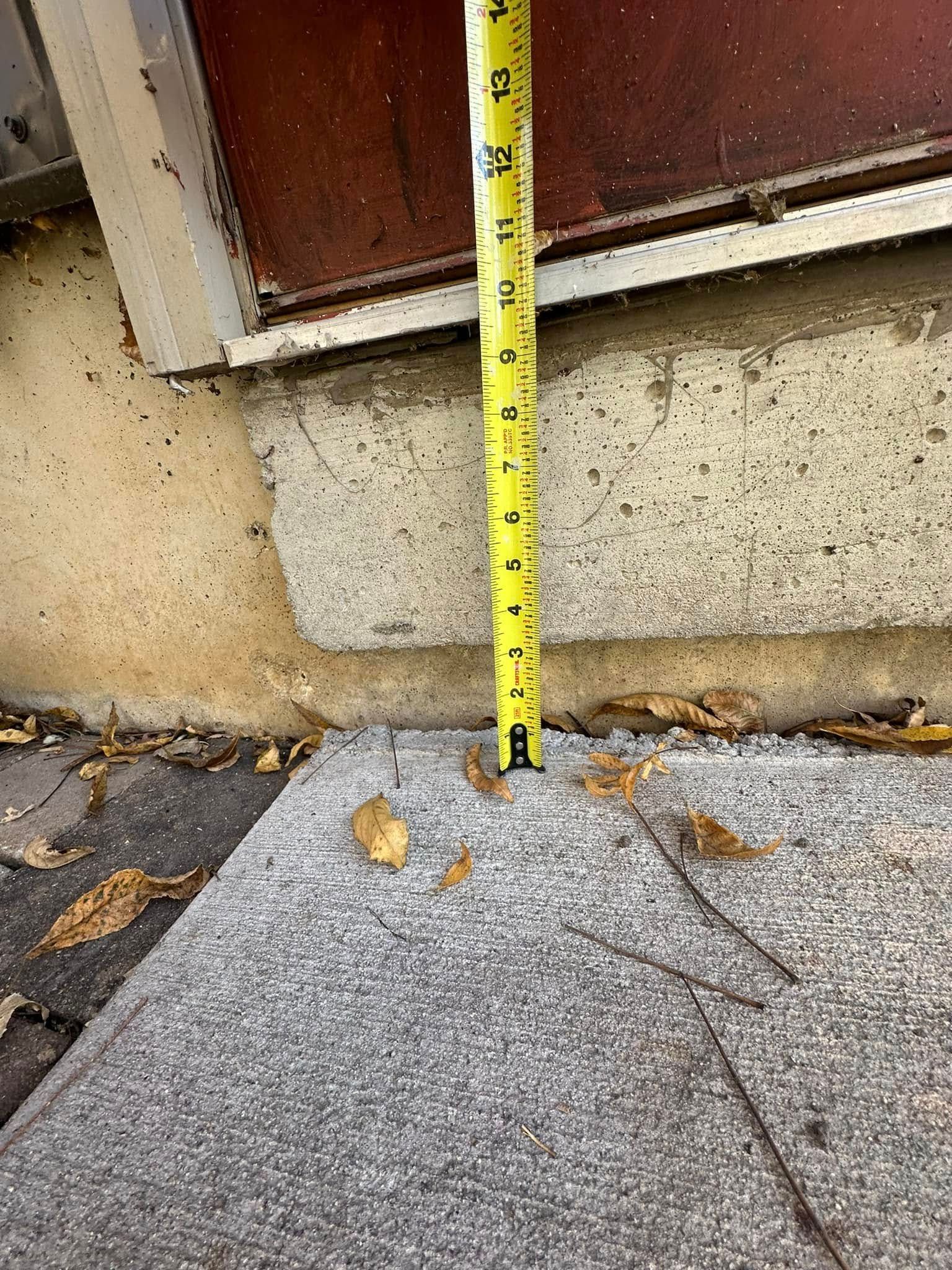 Tape measure showing a 2-inch height difference between a concrete slab and a building's base.
