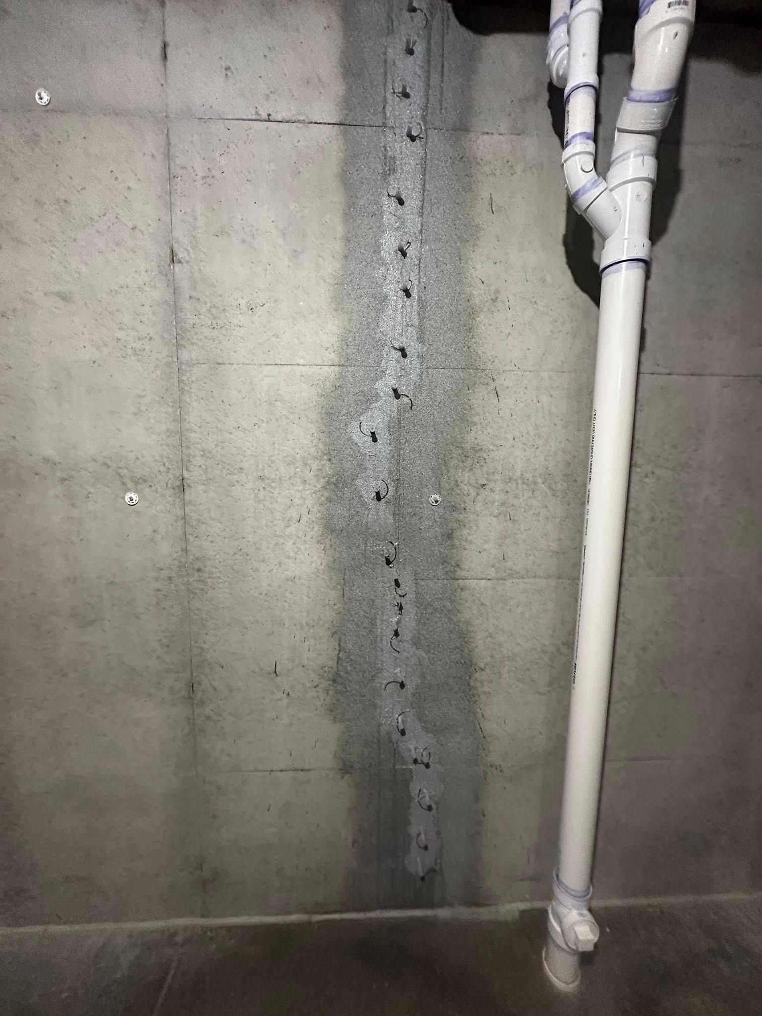 Concrete basement wall with vertical sealant, white plumbing pipes.