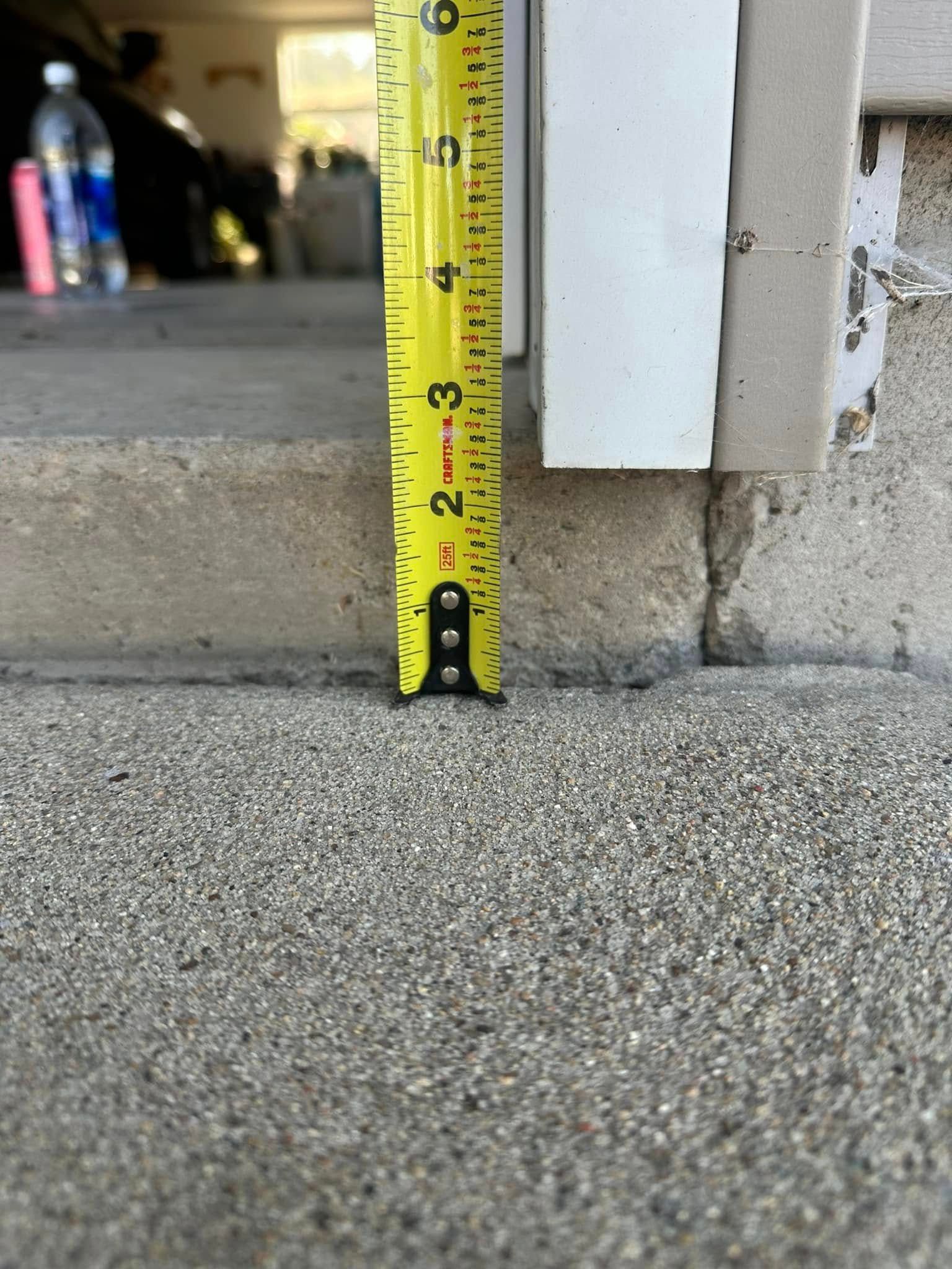 Tape measure showing a 2-inch height difference between concrete surfaces, likely a garage entryway.