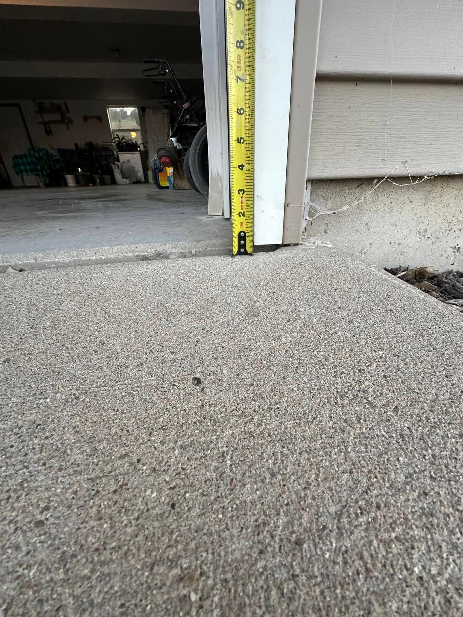 A yellow tape measure showing the height difference between a concrete slab and a doorway.
