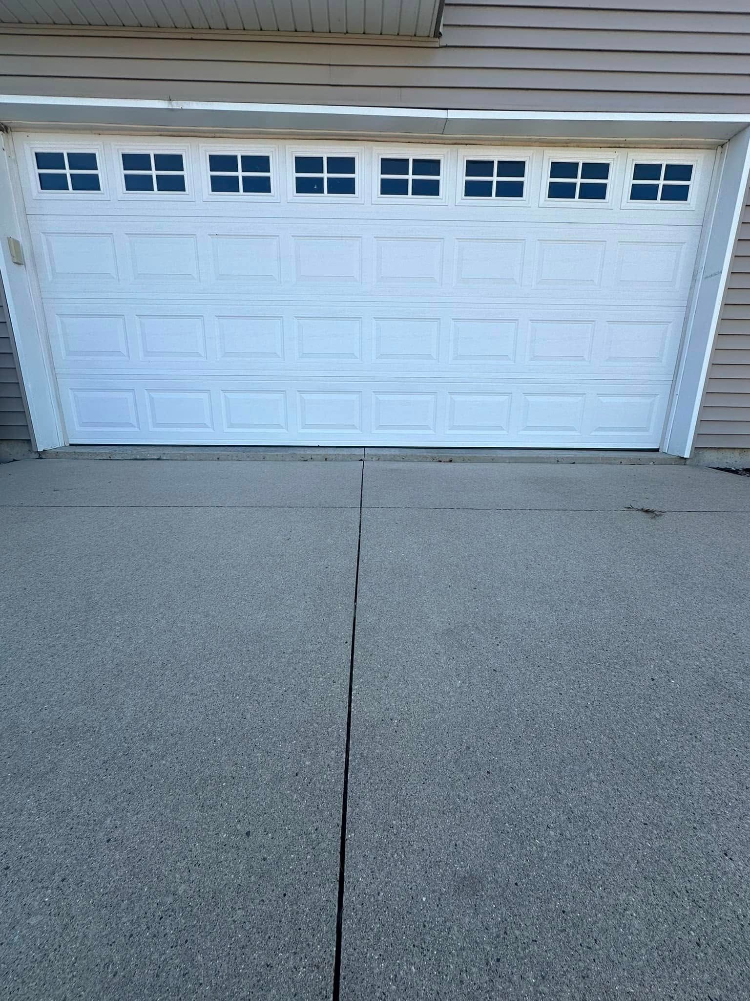 White garage door with multiple small windows above. Gray aggregate driveway.