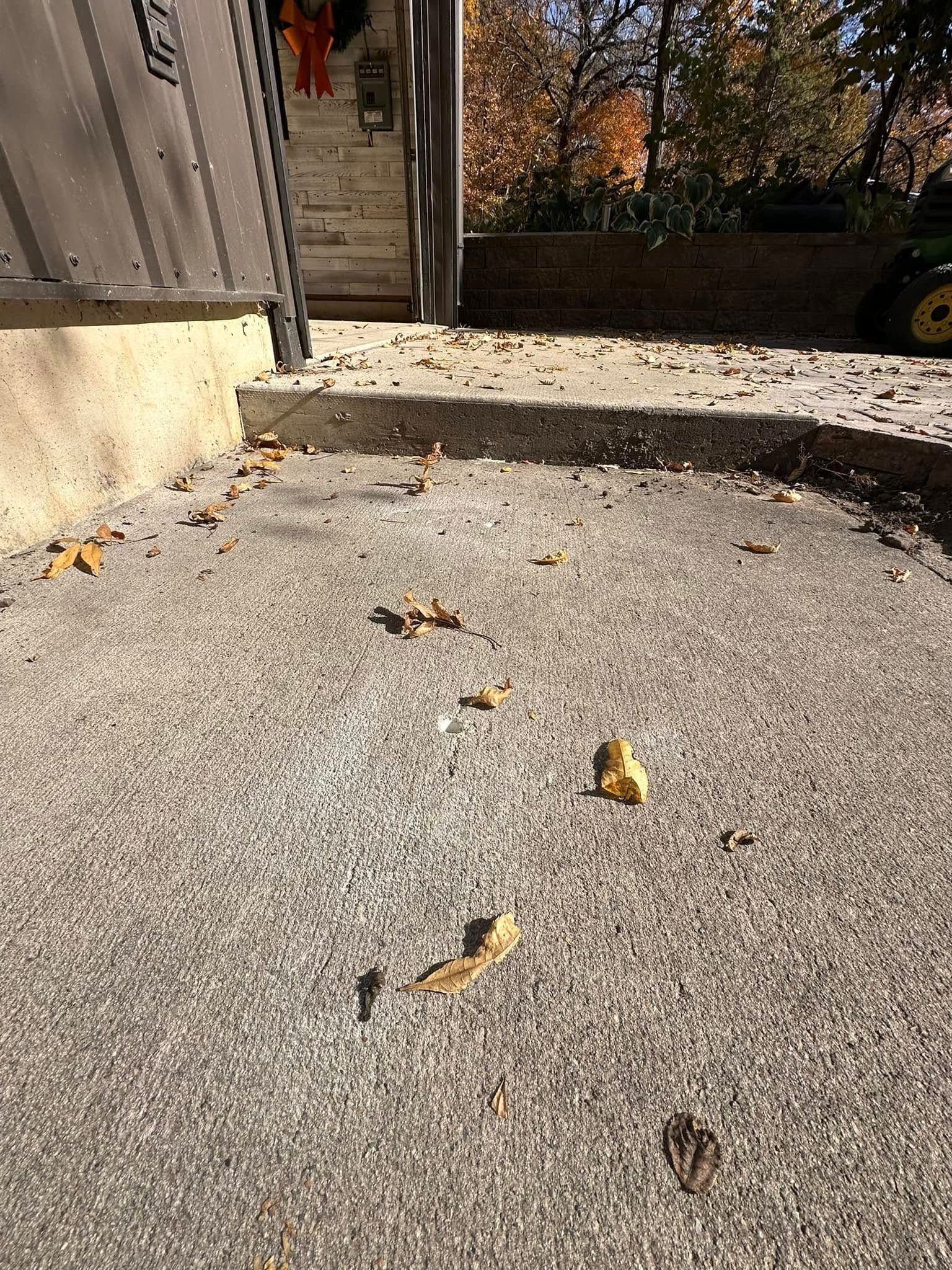 Concrete patio with fallen leaves, steps, and a glimpse of a lawnmower in a yard.