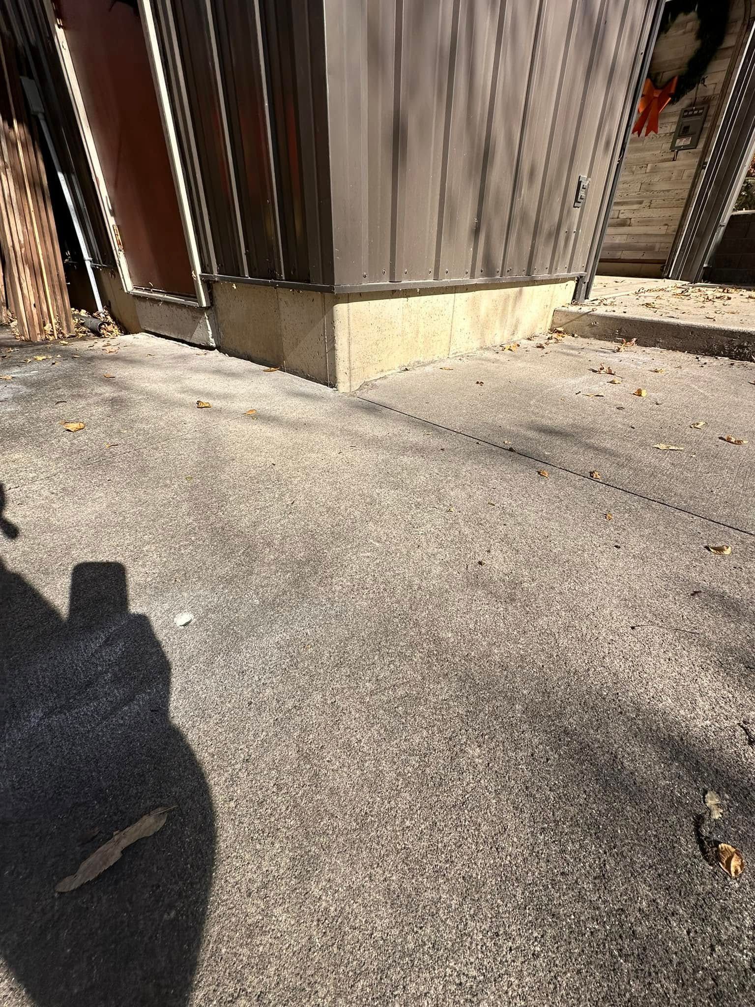 A concrete patio with a building's corner and shadow of a person holding a phone.