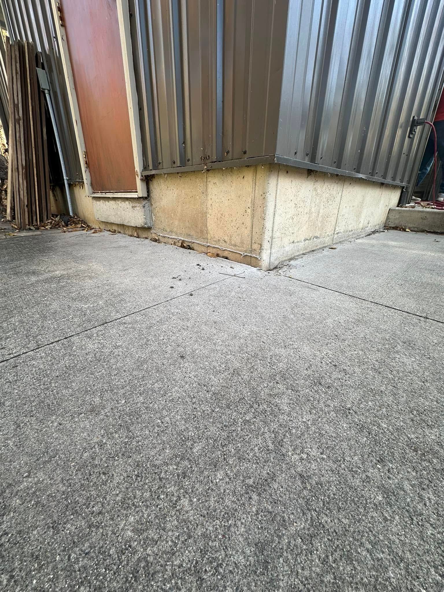 Brown and gray corrugated metal building corner on a gray textured concrete surface.