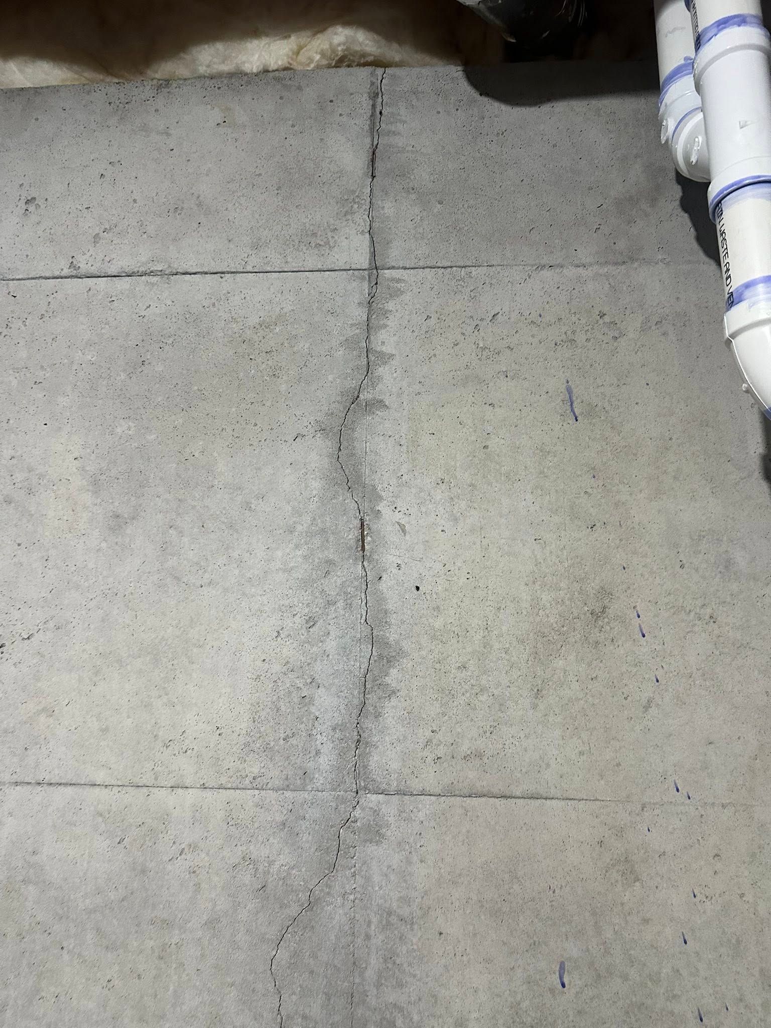 Concrete basement floor with marked grid lines, close up with white pipes in the upper right.