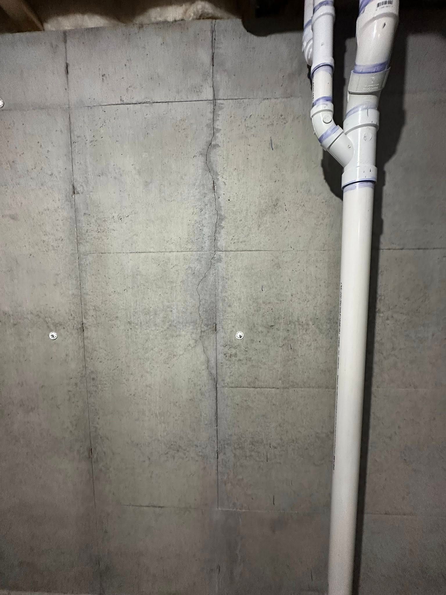Gray concrete basement wall with a vertical crack and white plumbing.