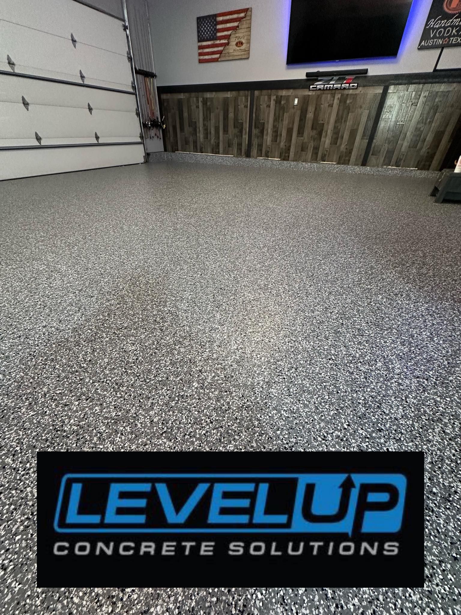 Garage floor with speckled gray coating, wall, and logo: Level Up Concrete Solutions.
