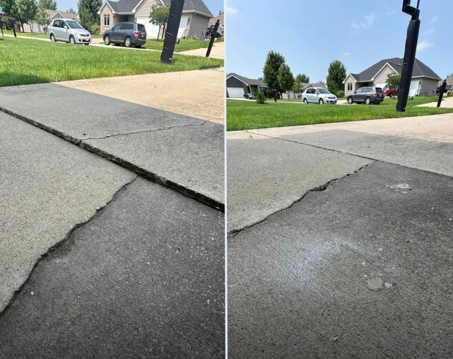 Cracked asphalt driveway meeting concrete sidewalk in a suburban neighborhood with houses and parked cars in the background