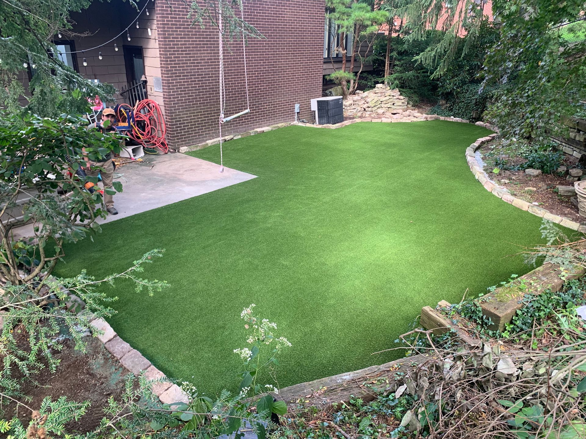 A backyard with a lush green lawn and a brick building in the background.