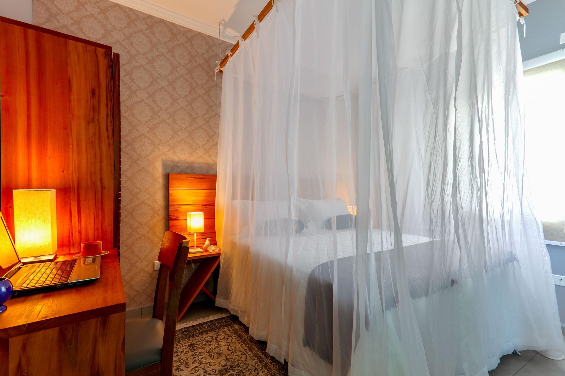 Quarto de hotel aconchegante com cama de dossel branca, luminárias em tons quentes e móveis de madeira.