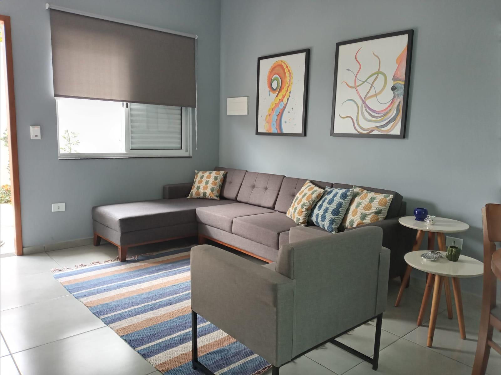 Sala de estar moderna com sofá modular cinza, tapete listrado, obras de arte na parede e mesas laterais junto à janela.