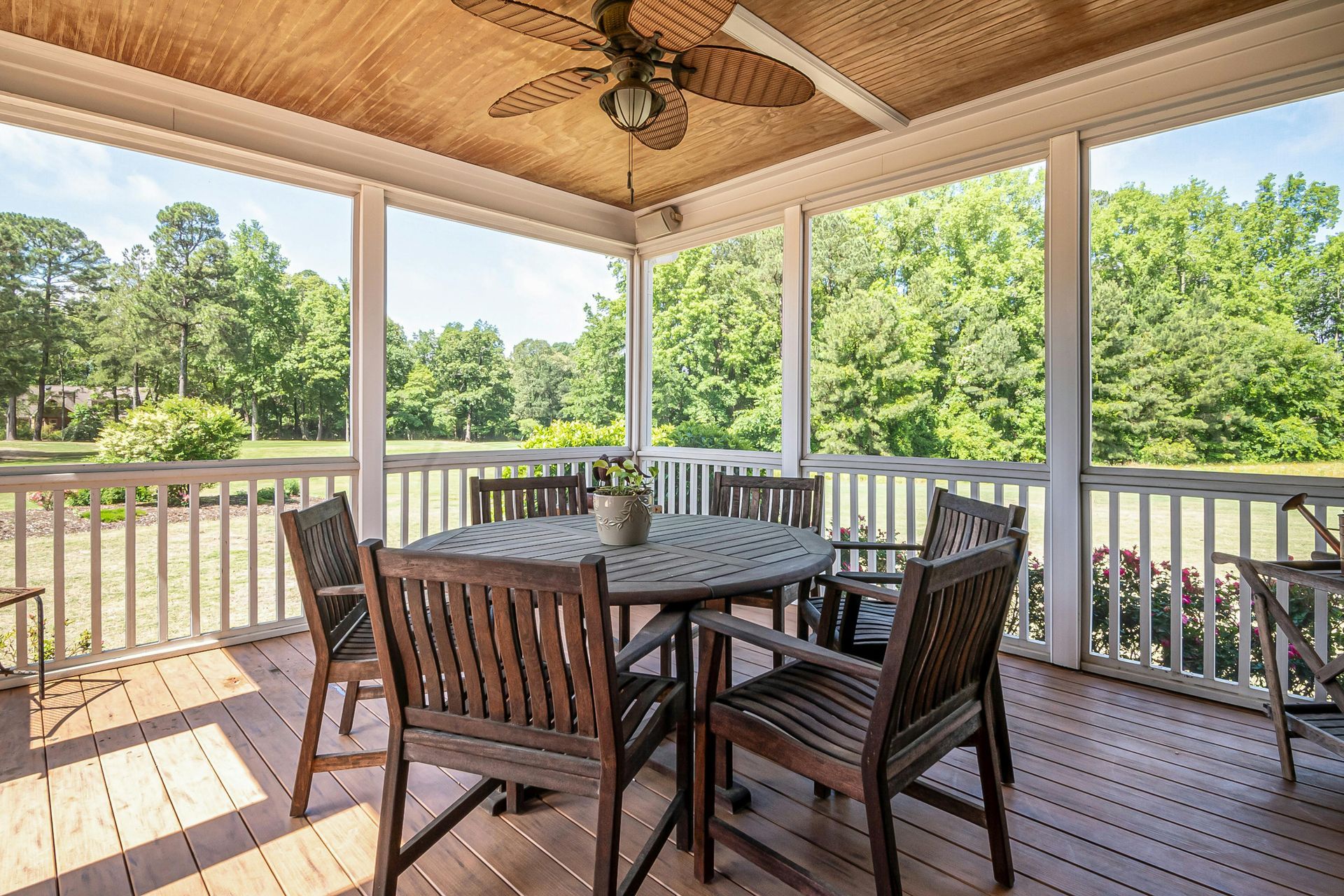 A screened in porch with a table and chairs and a ceiling fan.