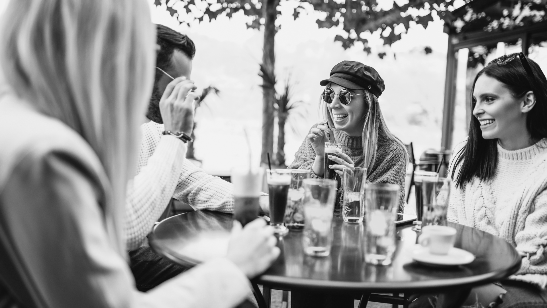 Friends at an outdoor cafe, laughing and drinking, in black and white.