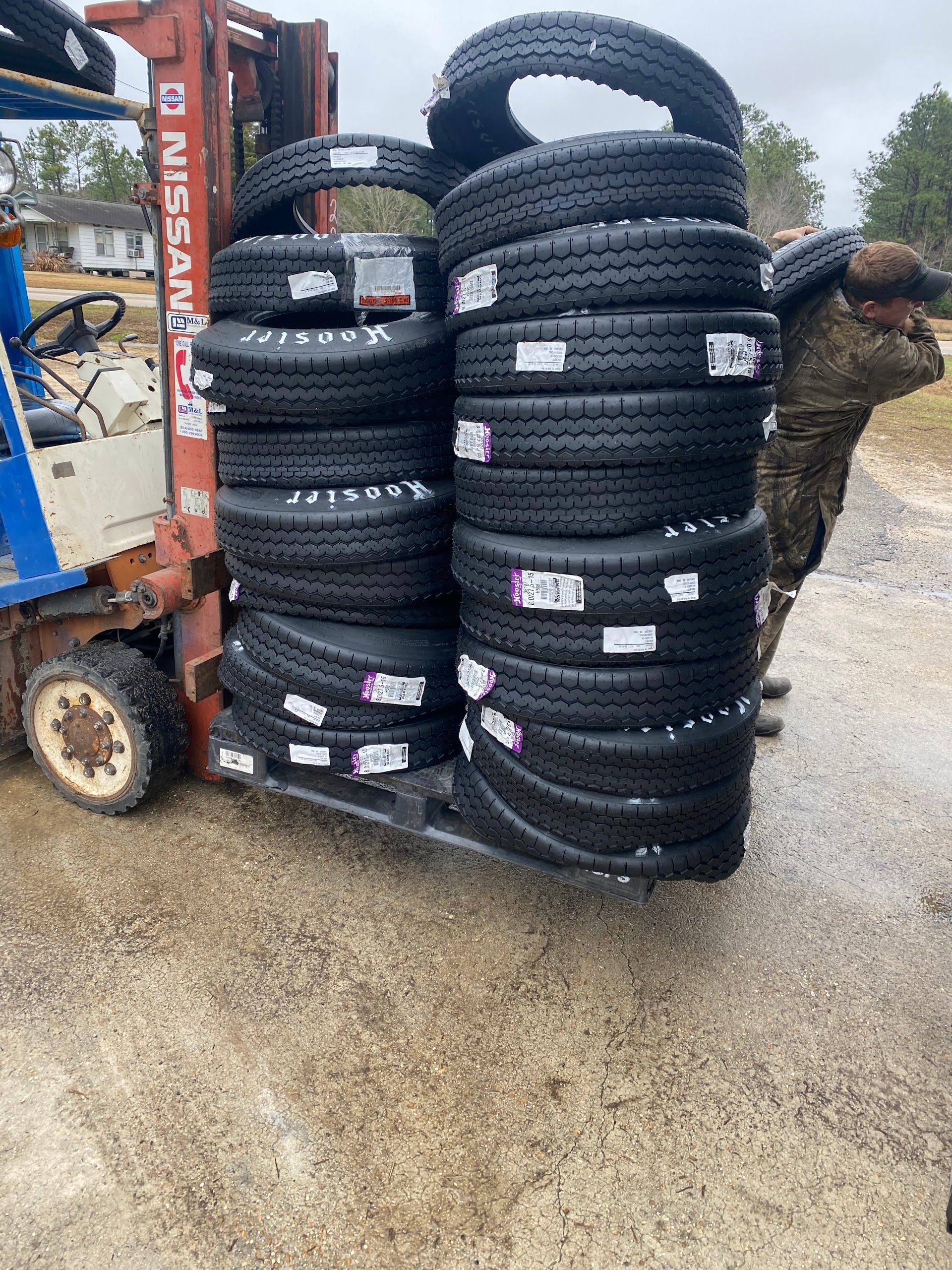 Forklift holding a large stack of new tires on a pallet, outdoors on a wet surface. | All Jacked Up