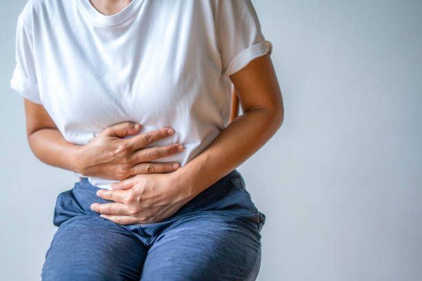 A Woman Is Sitting Down With Her Hands On Her Stomach – Dunbar, WV - Smith & Jones Chiropractic