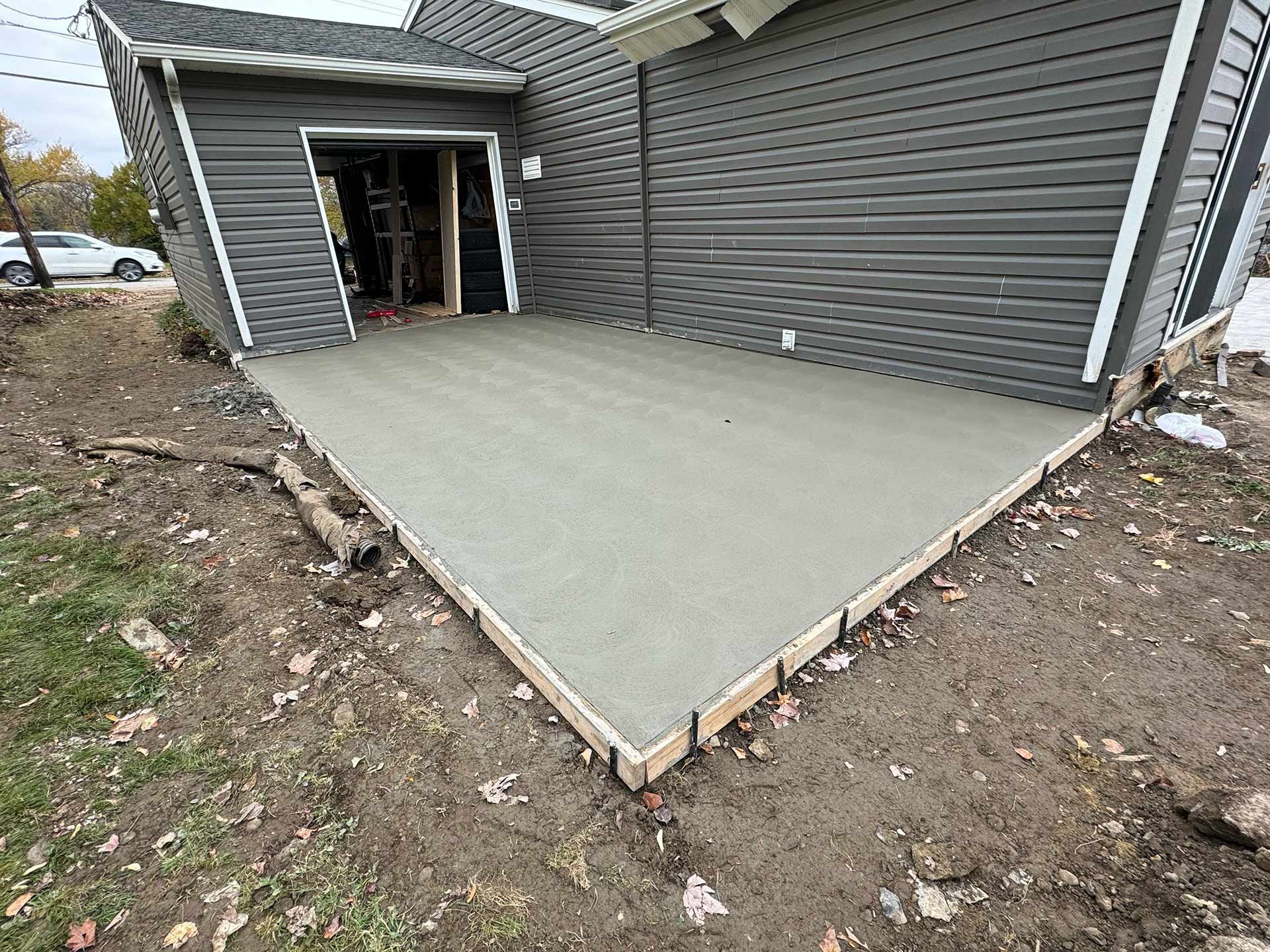Newly poured concrete patio next to a gray house, framed by wooden boards.