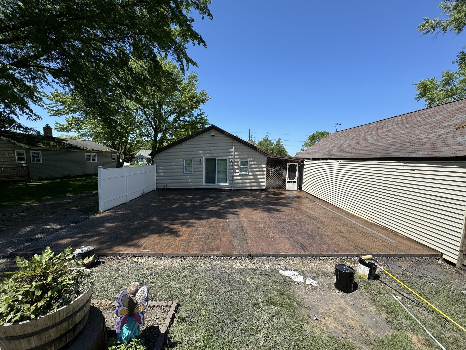 Backyard deck with dark wooden planks, white fence, and small shed under a blue sky.