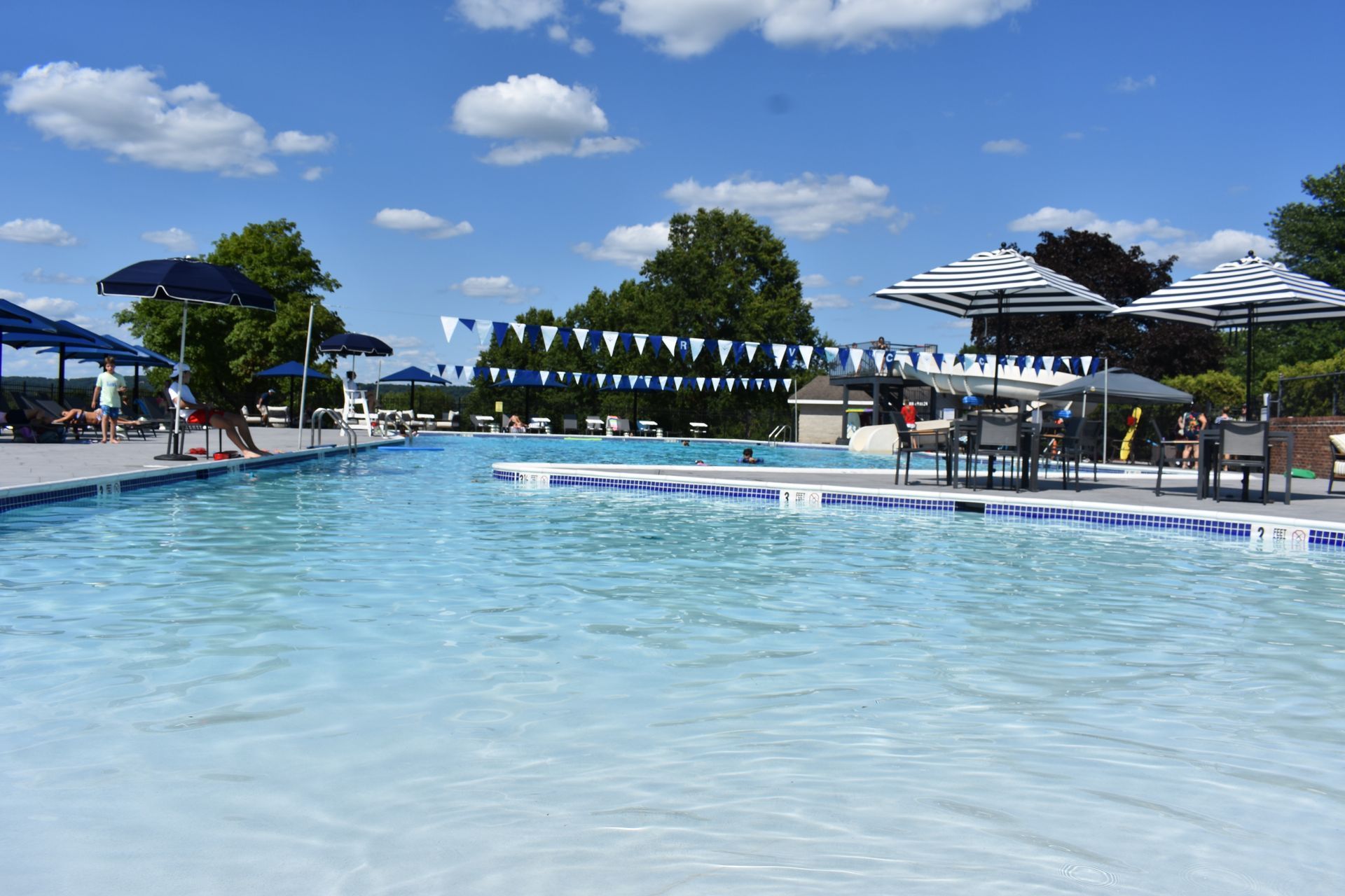 Outdoor swimming pool with clear blue water, umbrellas, and lounge chairs under a sunny sky
