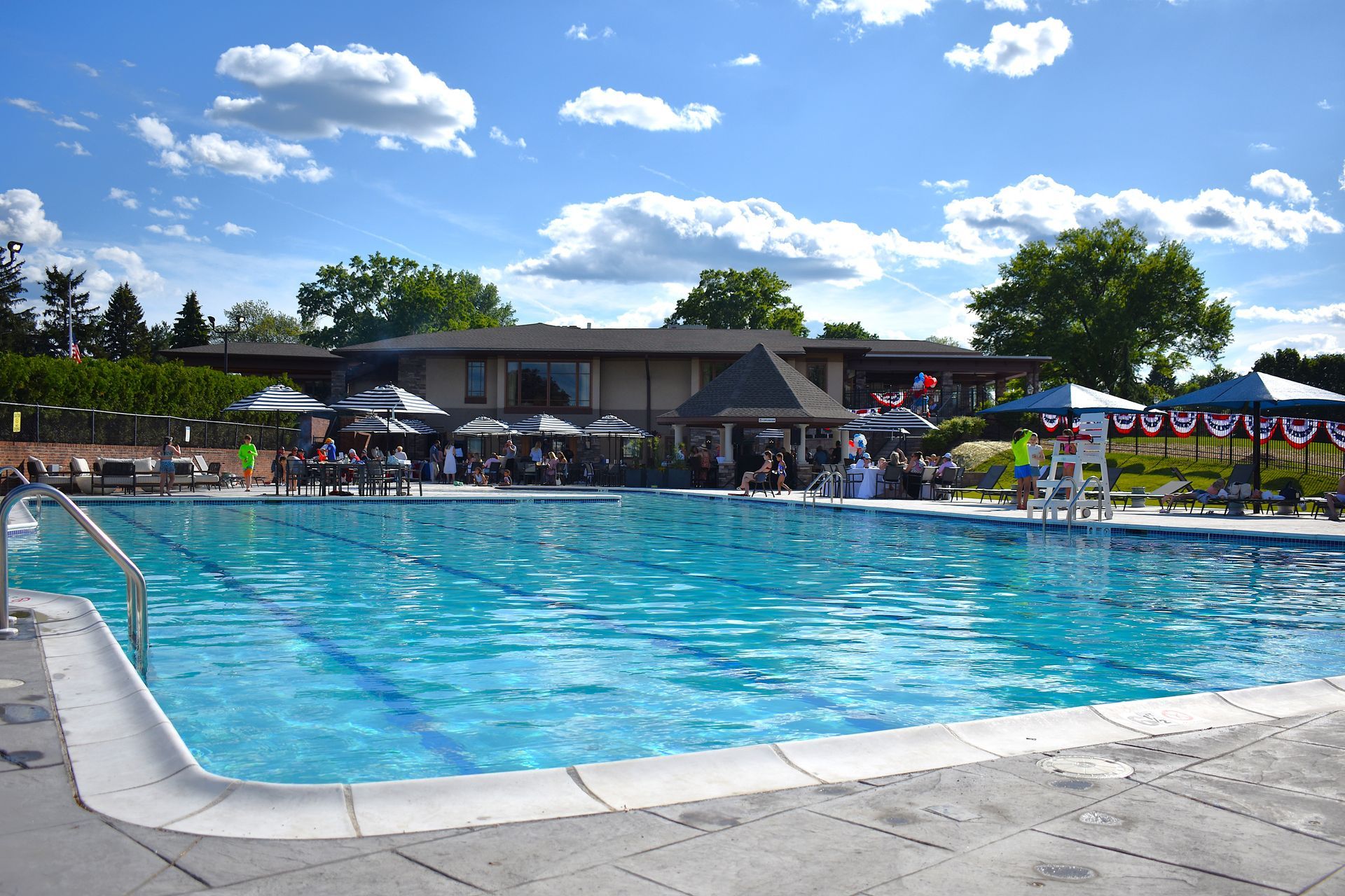 Outdoor swimming pool with people lounging under umbrellas on a sunny day