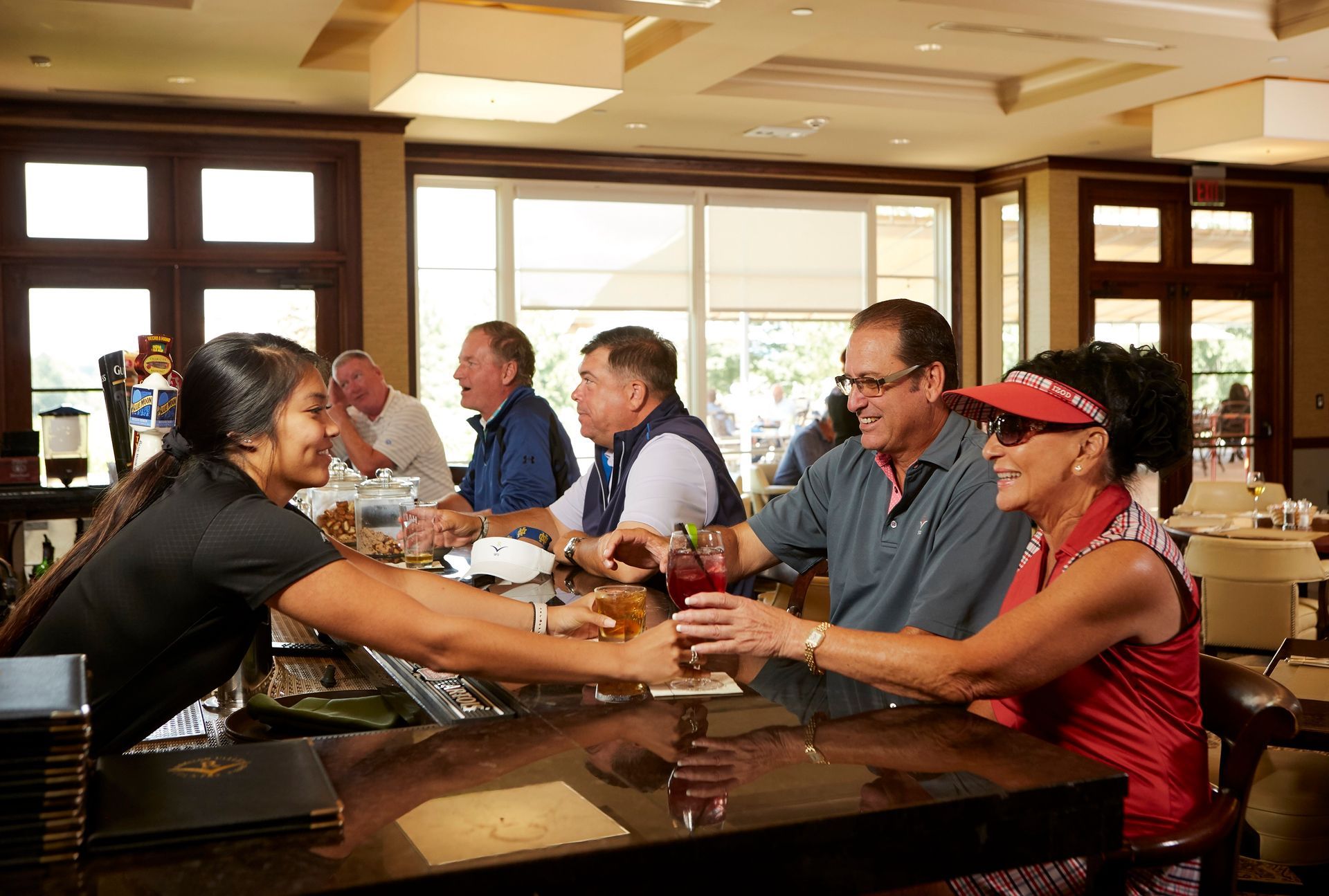 People chatting and drinking at a hotel bar with warm sunlight and large windows