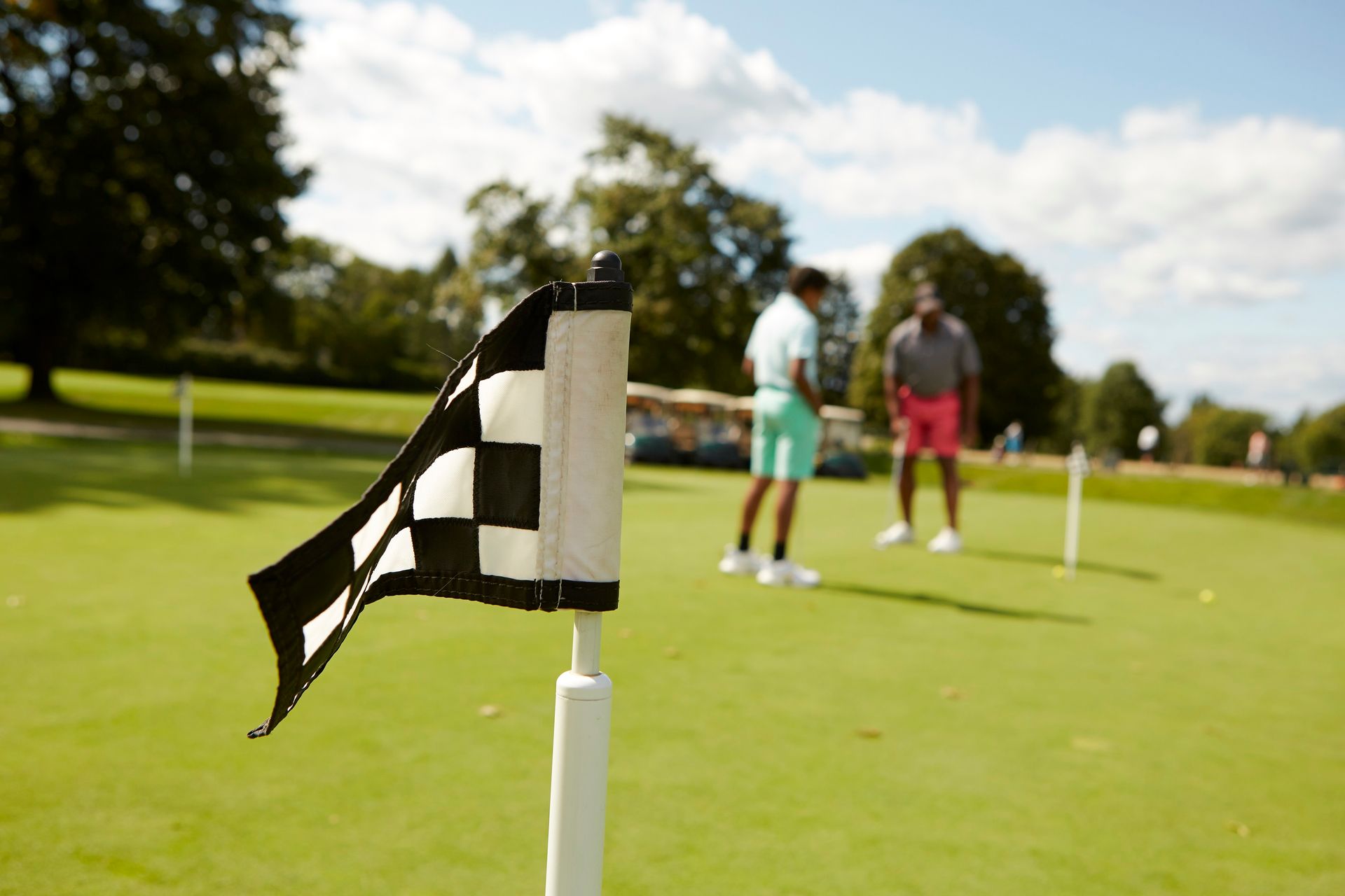 Golf putting green with flag in the foreground and two blurred players in the background