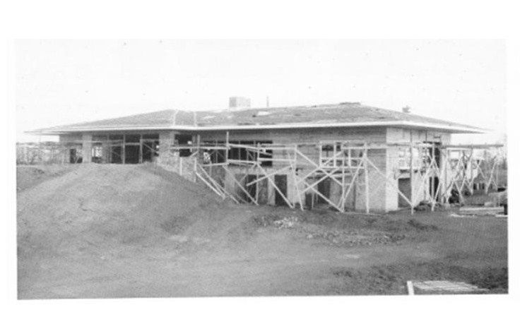 Black-and-white photo of a building under construction with scaffolding and dirt piles around it.