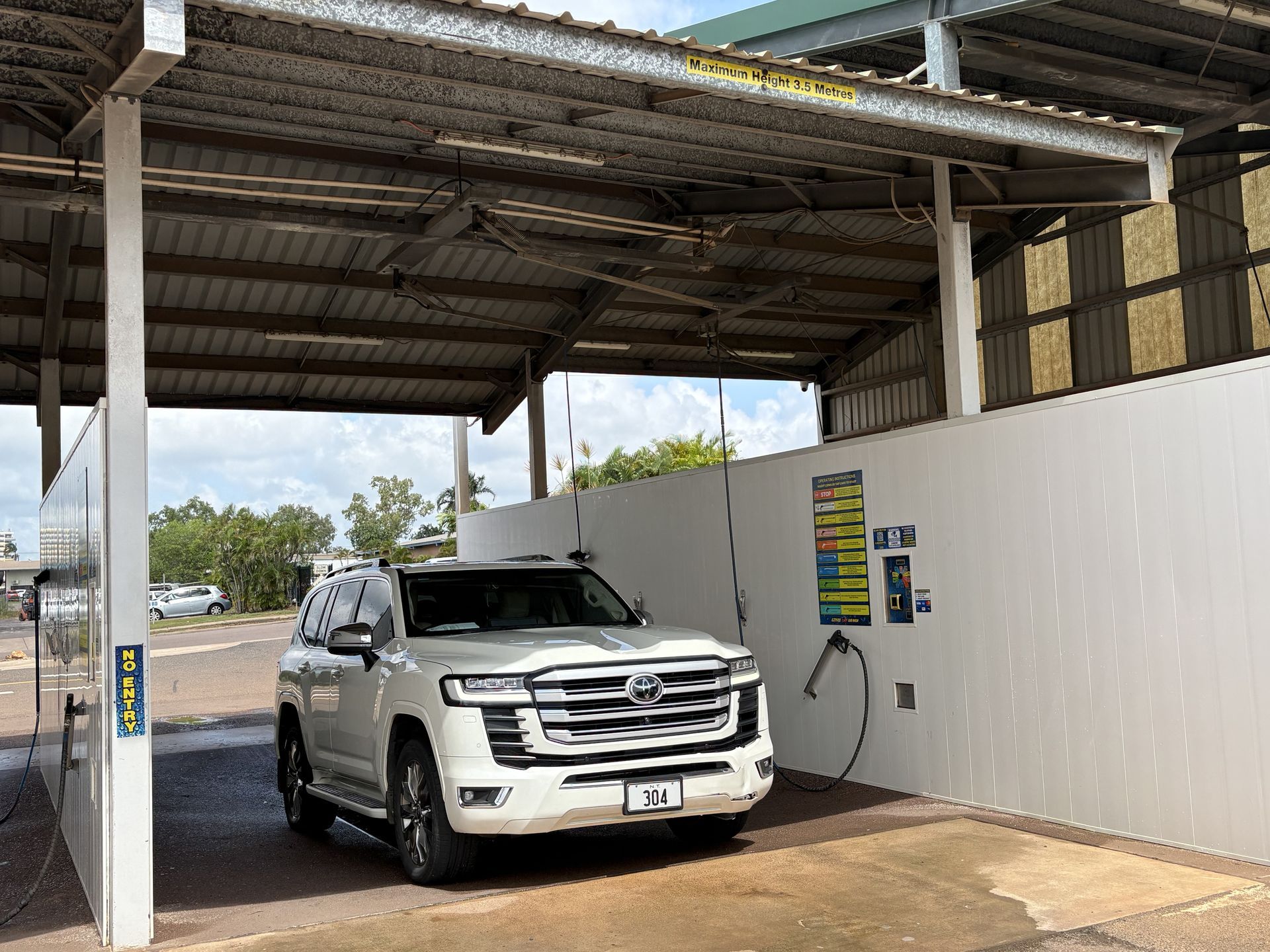 White SUV at a car wash bay under a metal roof, with a hose on the right wall. — Ezyas Car Wash NT in Yarrawonga, NT