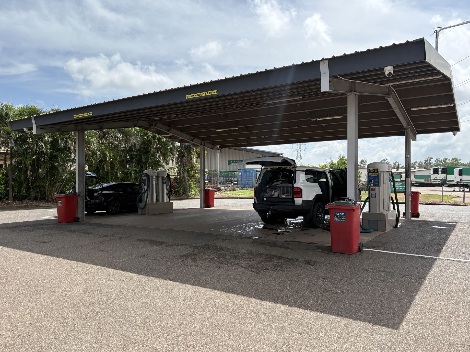 Covered parking area with two cars, red bins, and a gravel lot under a cloudy sky — Ezyas Car Wash NT in Yarrawonga, NT