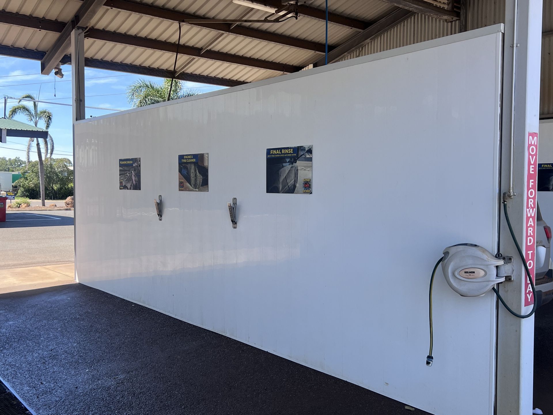 White industrial wall with small windows and hose reel under a metal-roofed shed, beside gravel ground — Ezyas Car Wash NT in Yarrawonga, NT