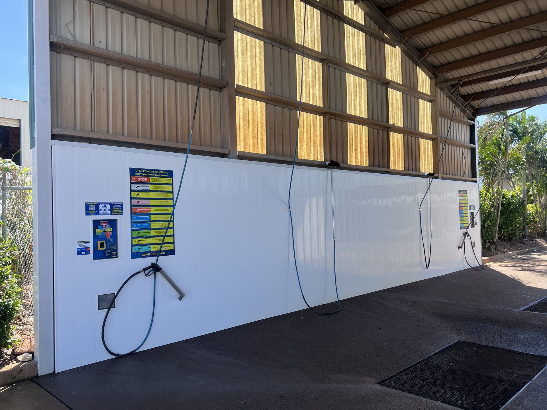 White building wall with colourful electrical panel, hose, and roofed industrial walkway. — Ezyas Car Wash NT in Yarrawonga, NT