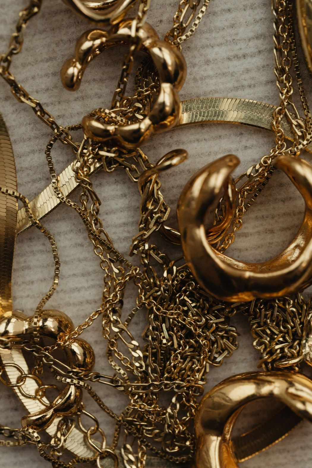 Catene d'oro e grossi anelli d'oro intrecciati su uno sfondo di tessuto a righe chiare.