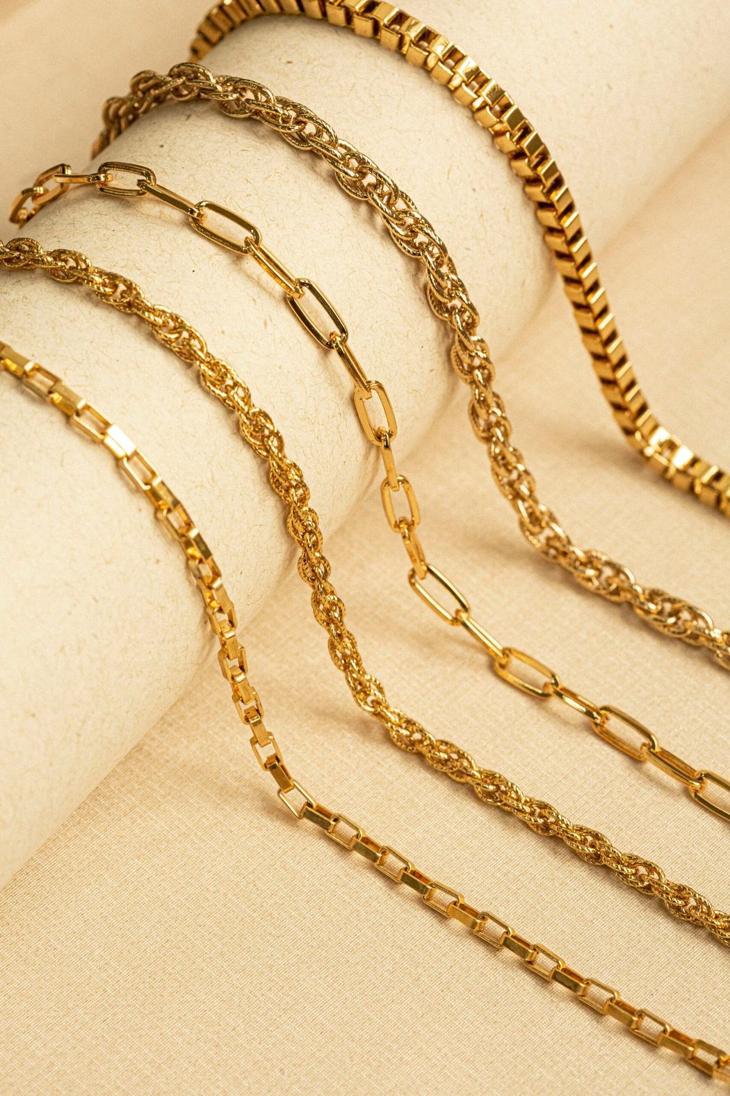 Diverse collane a catena d'oro disposte su una superficie beige.