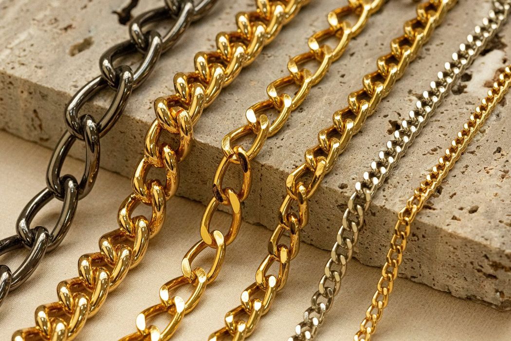 Collane a catena d'oro e d'argento disposte su una superficie di pietra beige.