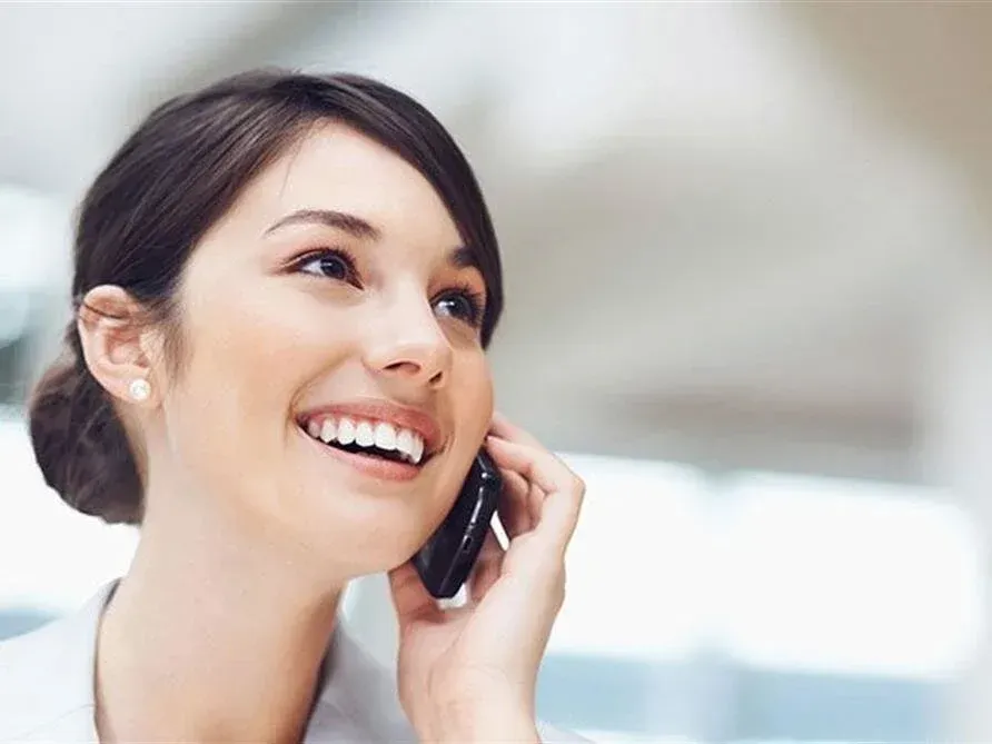 Smiling woman talking on a phone, wearing pearl earrings in a bright indoor setting