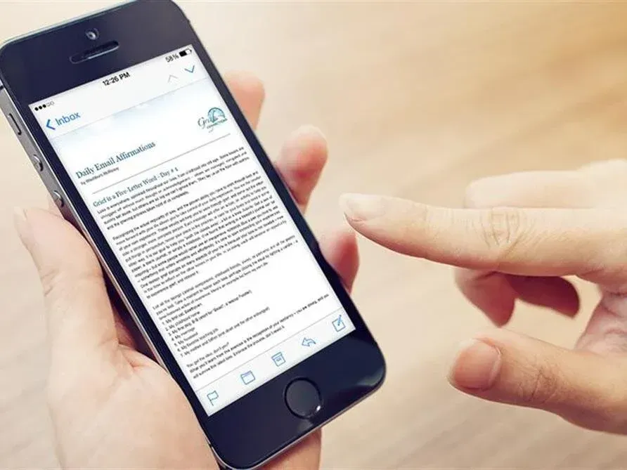 Hand holding a smartphone while another finger points at the screen showing a text message.