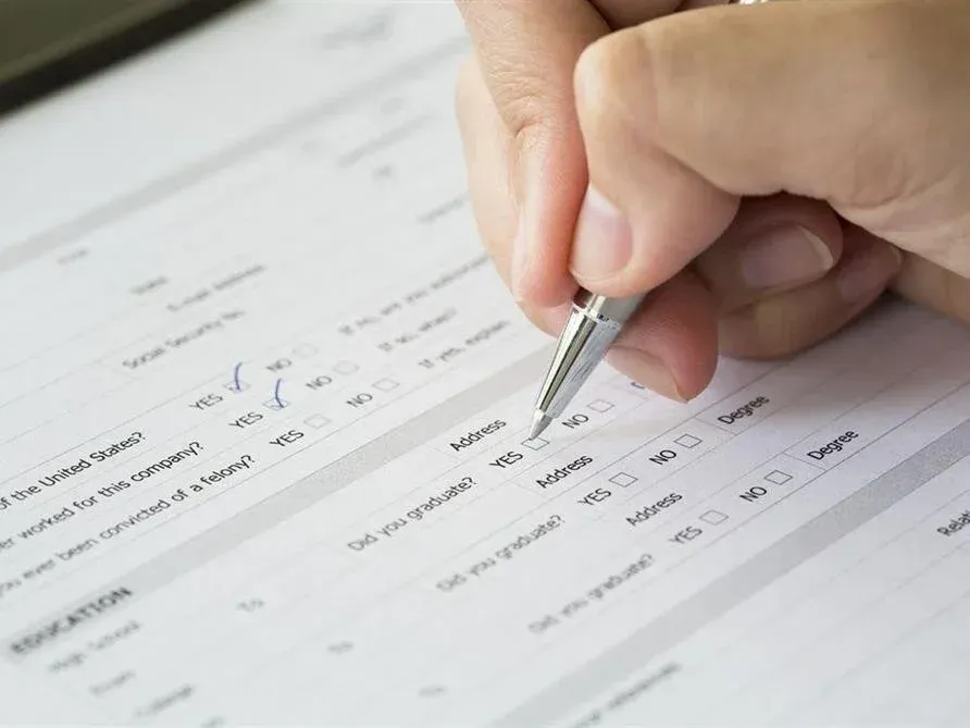 Hand filling out a form with a pen on a white document