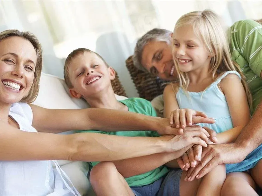 Family smiling together on a couch, stacking hands in a cozy living room.