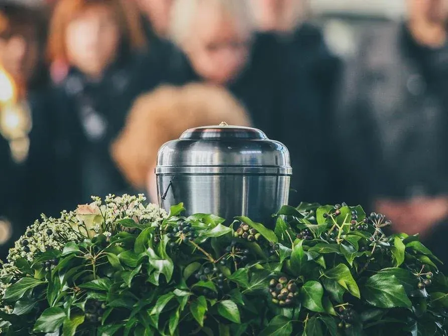 A shiny metal urn sitting in green foliage with a blurred crowd in the background