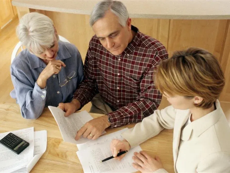 Three people reviewing documents at a wooden table with a calculator in a meeting room