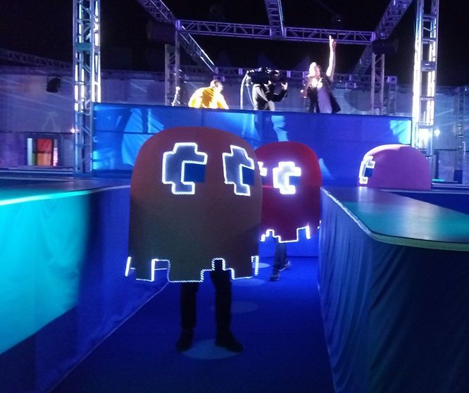 People in Pac-Man ghost costumes in an obstacle course with people on a platform in the background.