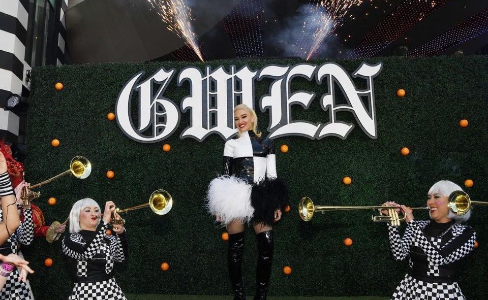 Gwen Stefani in a black and white outfit with trumpet players. Green backdrop with
