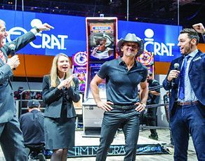 Country singer Tim McGraw at a slot machine launch with excited staff at a trade show booth.
